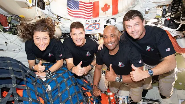 Foto dos quatro tripulantes da Artemis 2, com o polegar para cima, flutuando no interior da espaçonave