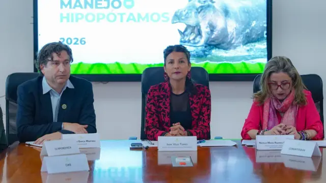 A ministra do Meio Ambiente (no centro) sentada em uma mesa durante o anúncio do plano de governo para reduzir a população de hipopótamos.