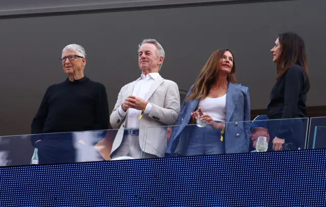 Bill Gates e outras três pessoas do alto de um camarote vendo o jogo no estádio