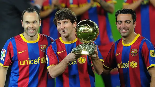 Messi (centro) segura o troféu Bola de Ouro de 2010, ao lado de Iniesta (esq.) e Xavi (dir.), todos vestindo camisas do Barcelona