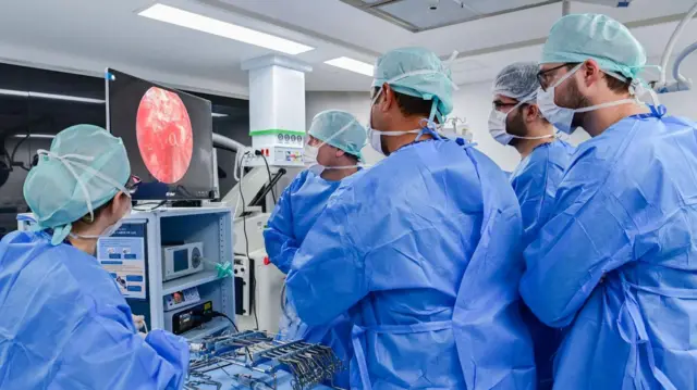 Médicos olham para uma tela enquanto fazem uma cirurgia