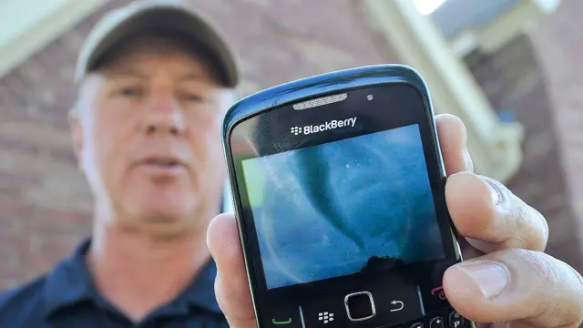 Um homem de boné mostra o registro de um tornado na tela de seu celular da marca BlackBerry, em Denton, Texas, em 2011