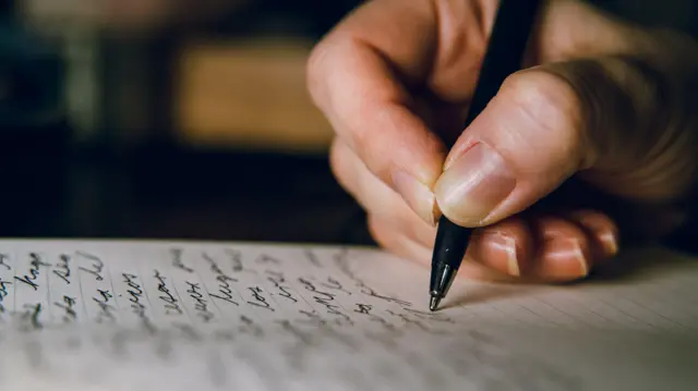 Mão escreve com caneta em um caderno pautado