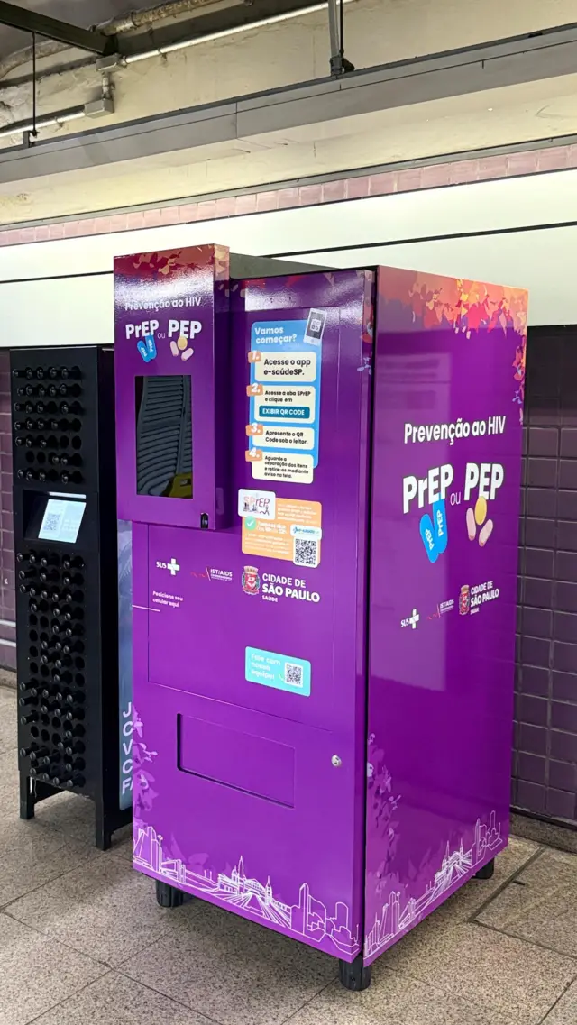 A imagem mostra uma máquina automática de distribuição de medicamentos para prevenção do HIV instalada em uma estação de metrô de São Paulo. Com acabamento roxo e identificação da Prefeitura de São Paulo e do SUS, o equipamento exibe instruções para retirada de PrEP e PEP por meio do aplicativo e-saúdeSP e de um QR Code.