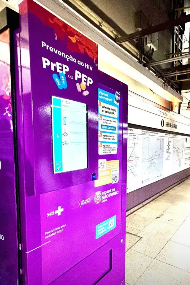 A imagem mostra uma máquina automática de distribuição de medicamentos para prevenção do HIV instalada em uma estação de metrô de São Paulo. Com acabamento roxo e identificação da Prefeitura de São Paulo e do SUS, o equipamento exibe instruções para retirada de PrEP e PEP por meio do aplicativo e-saúdeSP e de um QR Code.