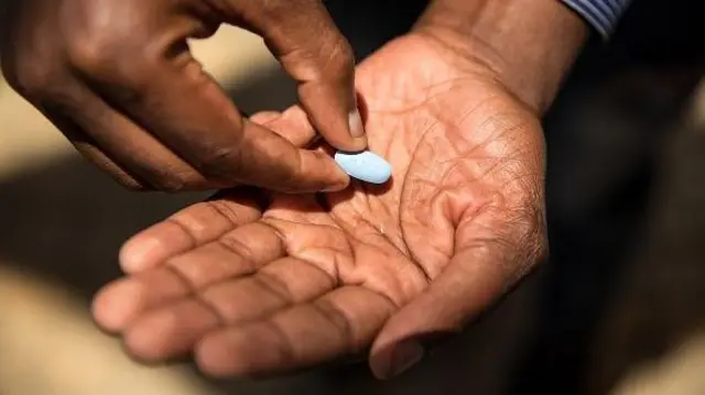 Pessoa recebendo comprimido azul de PrEP na mão.
